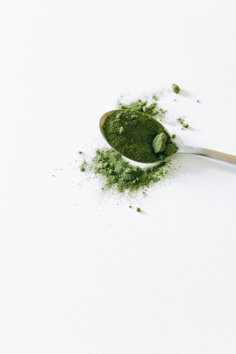 A spoonful of green cardamom powder is scattered on a white background.