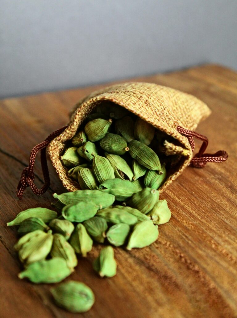 A bag filled with green cardamom pods sitting on top of a wooden table