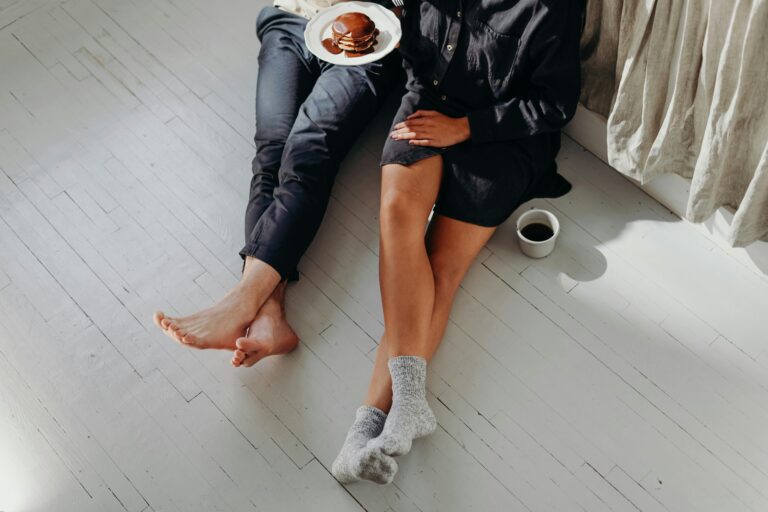 a man and woman sitting on the floor eating cake