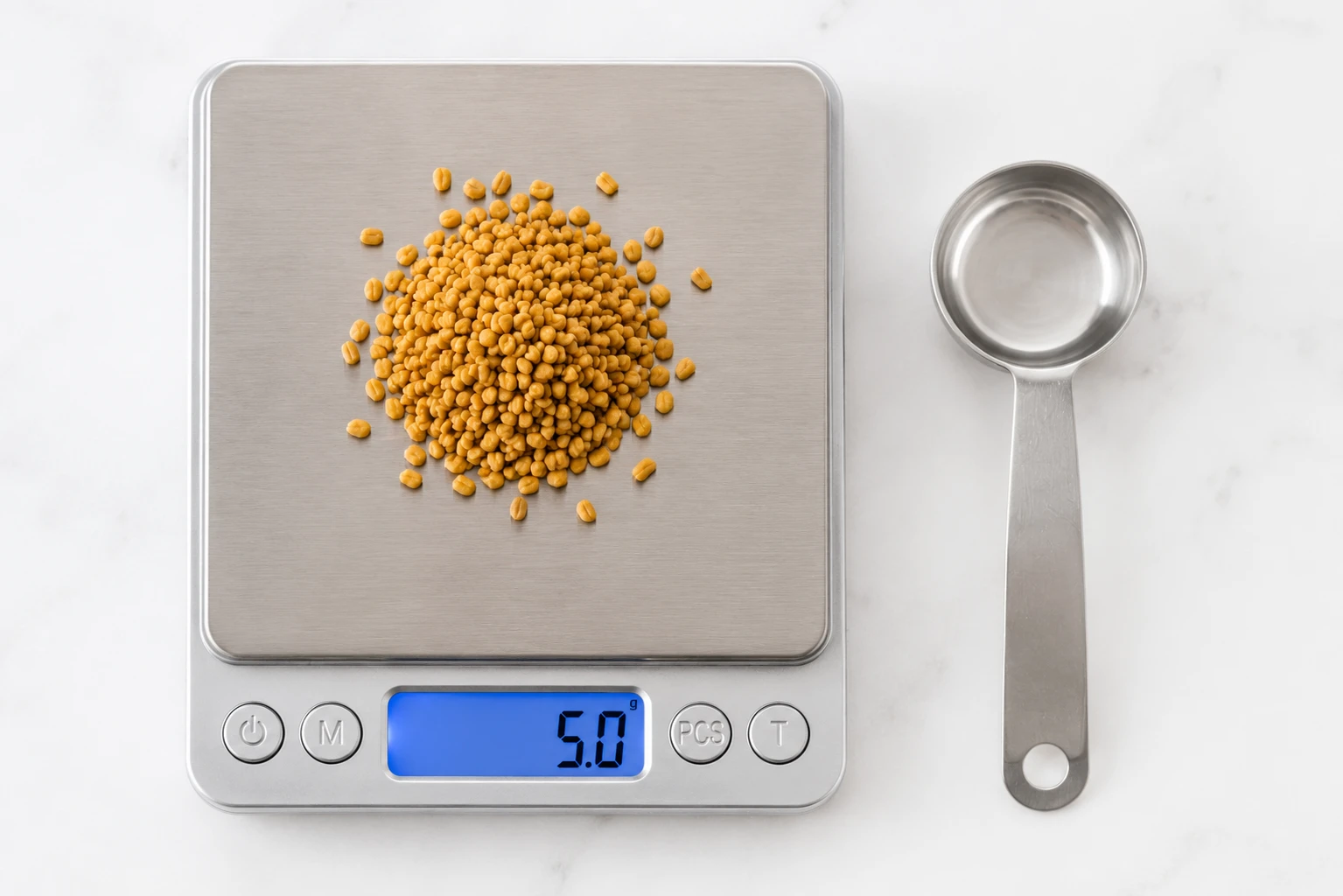 Digital kitchen scale measuring 5 grams of fenugreek seeds with measuring teaspoon on white background
